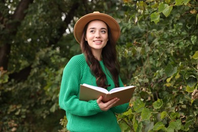 Beautiful young woman in stylish warm sweater reading book outdoors