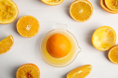 Photo of Squeezer and cut fresh oranges on white wooden table, flat lay