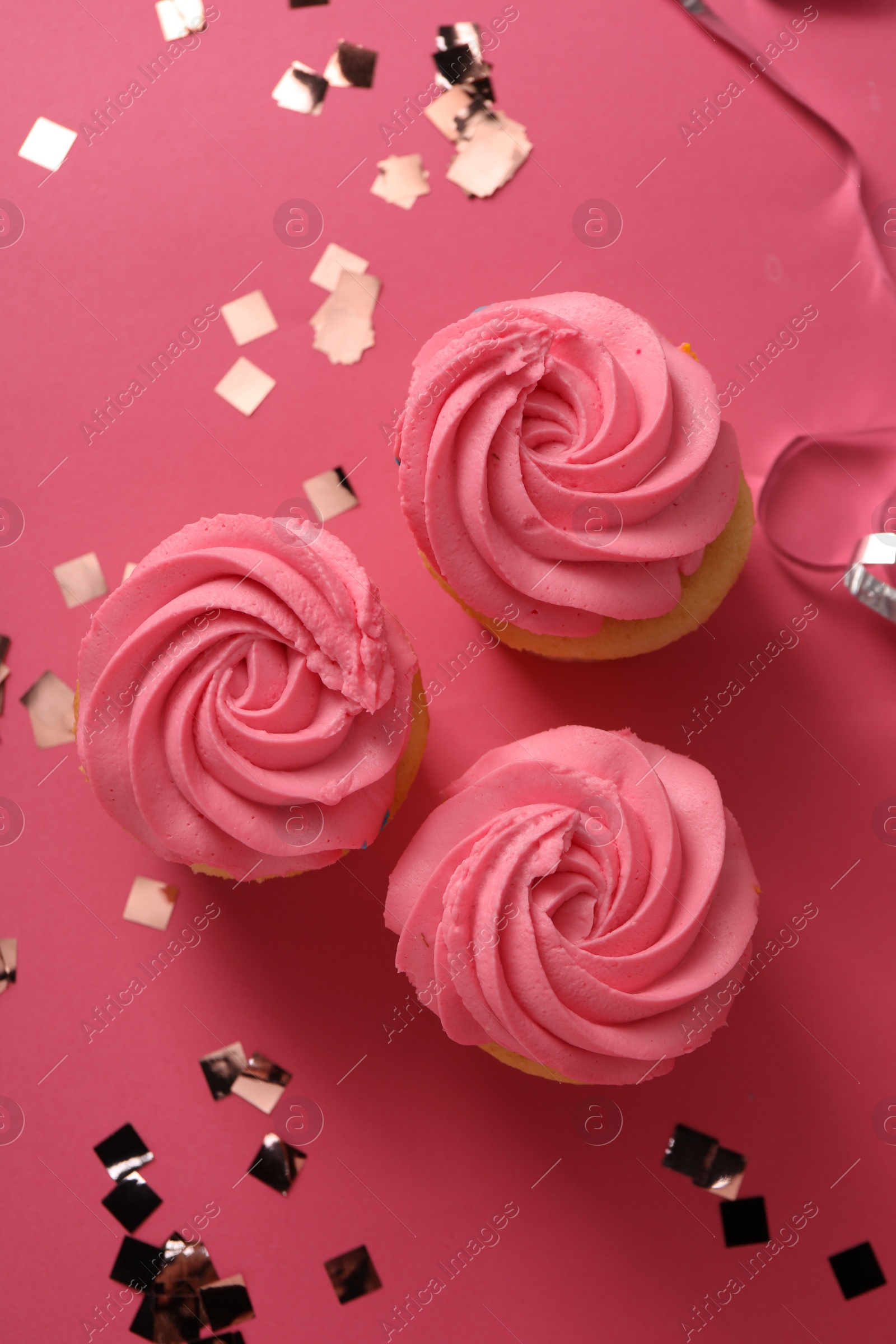 Photo of Delicious cupcakes with bright cream and confetti on pink background, flat lay