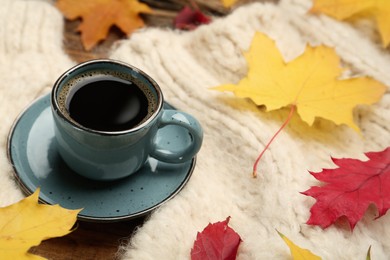 Photo of Cup of hot coffee, sweater and autumn leaves on table, space for text
