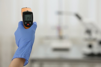 Photo of Closeup view of doctor with infrared thermometer on blurred background, space for text. Checking temperature during Covid-19 pandemic