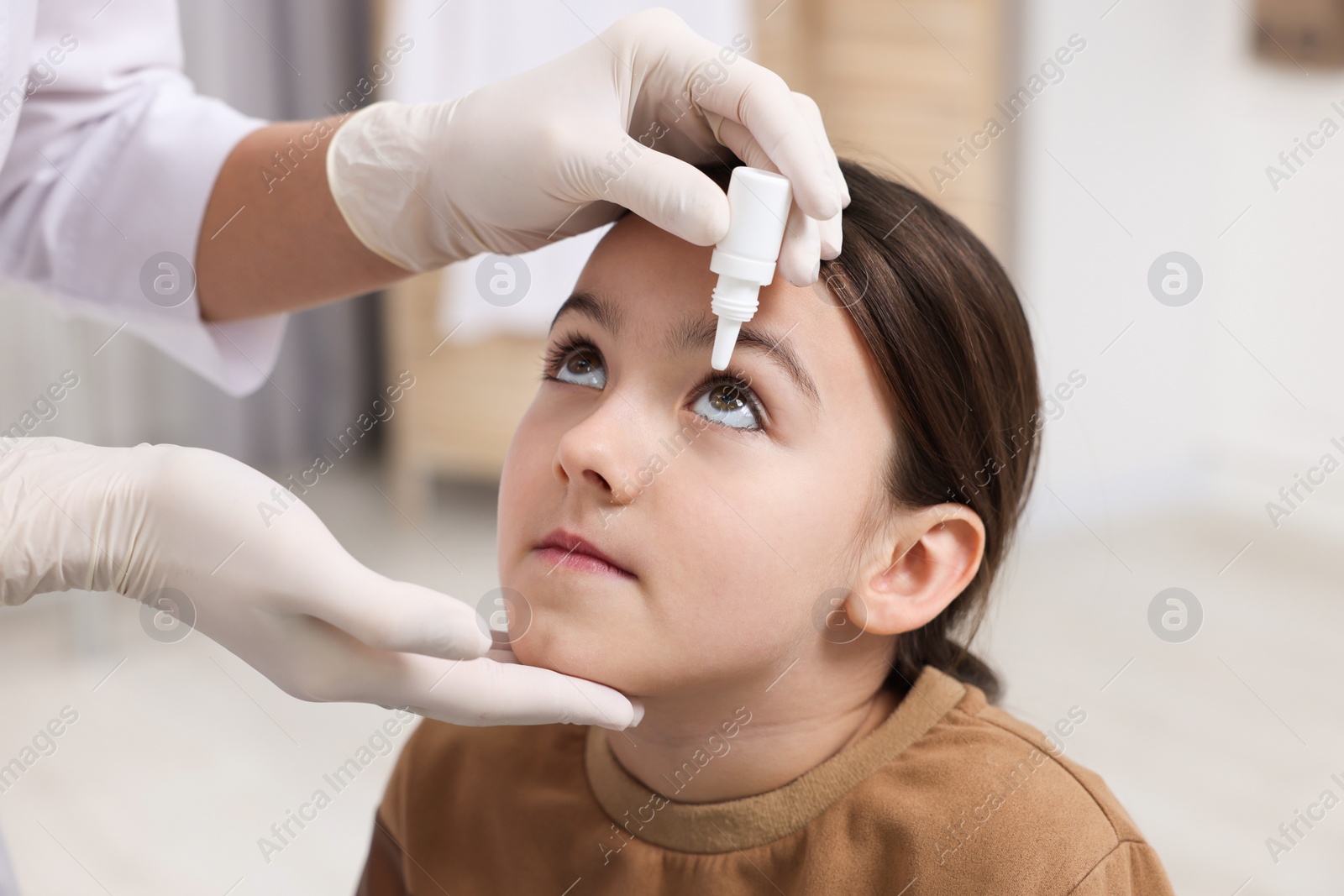 Photo of Doctor applying medical drops into girl's eye indoors