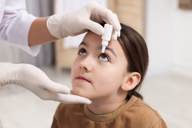 Doctor applying medical drops into girl's eye indoors