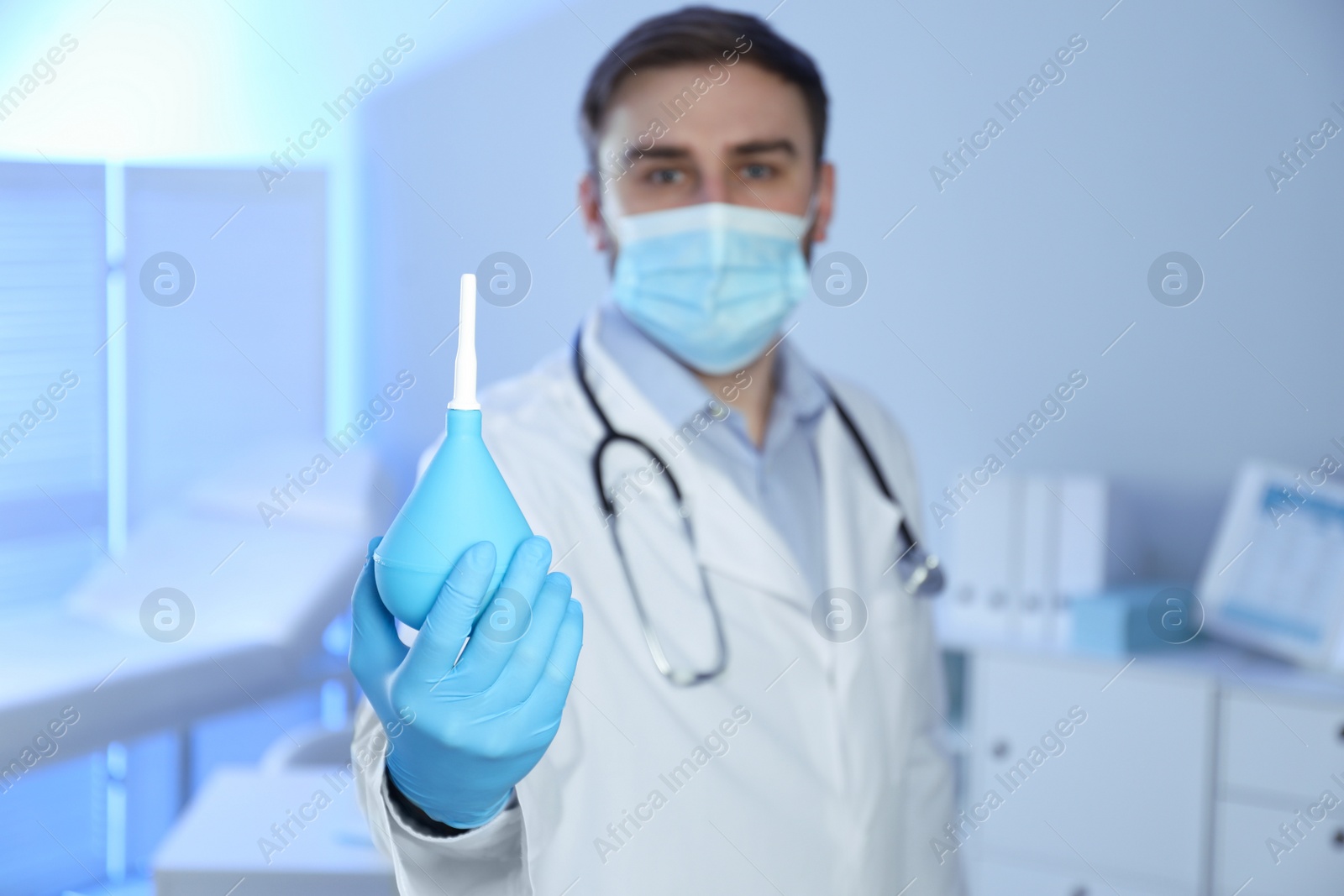 Photo of Doctor holding rubber enema in examination room, focus on hand. Space for text