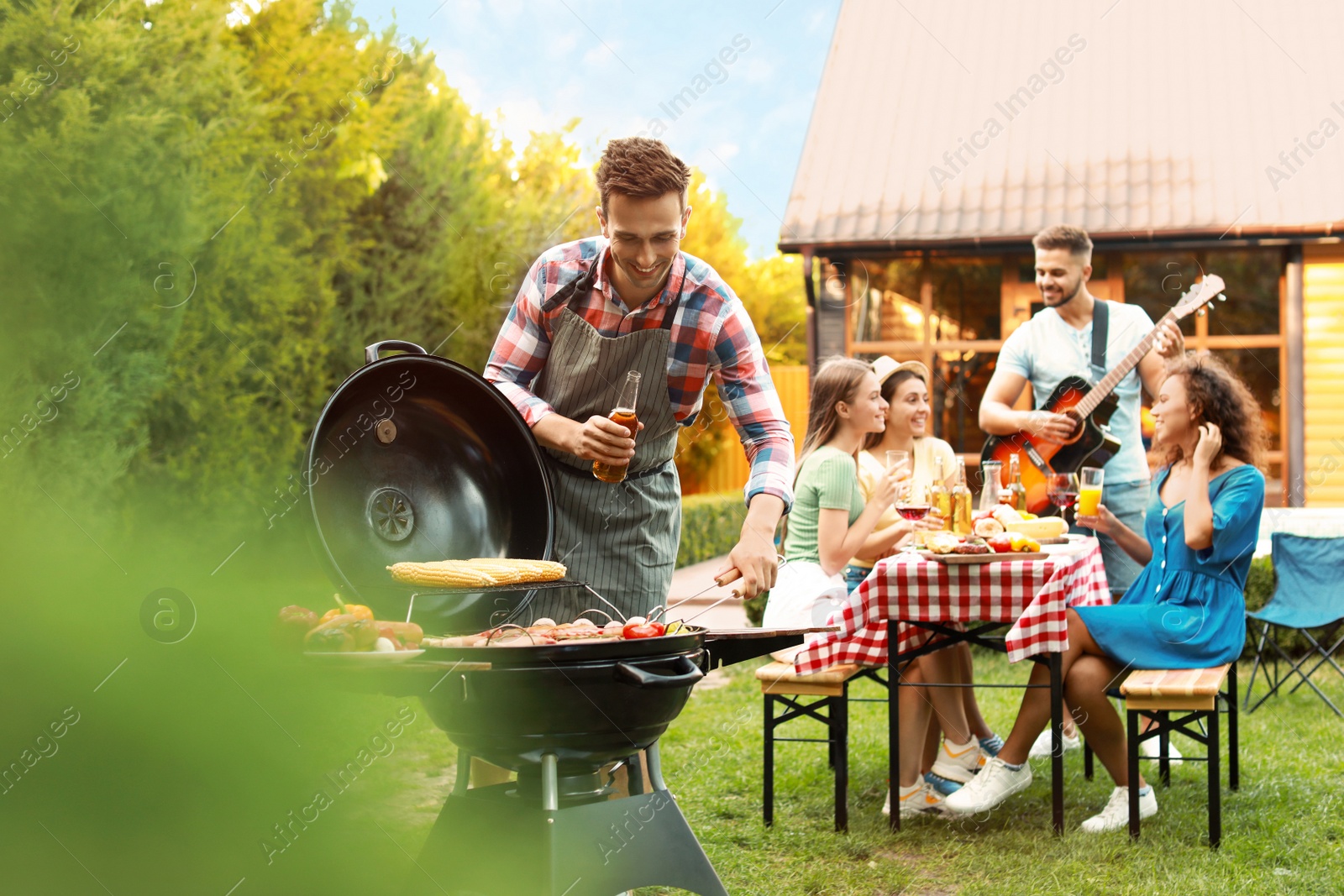 Photo of Group of friends at barbecue party outdoors. Young man near grill