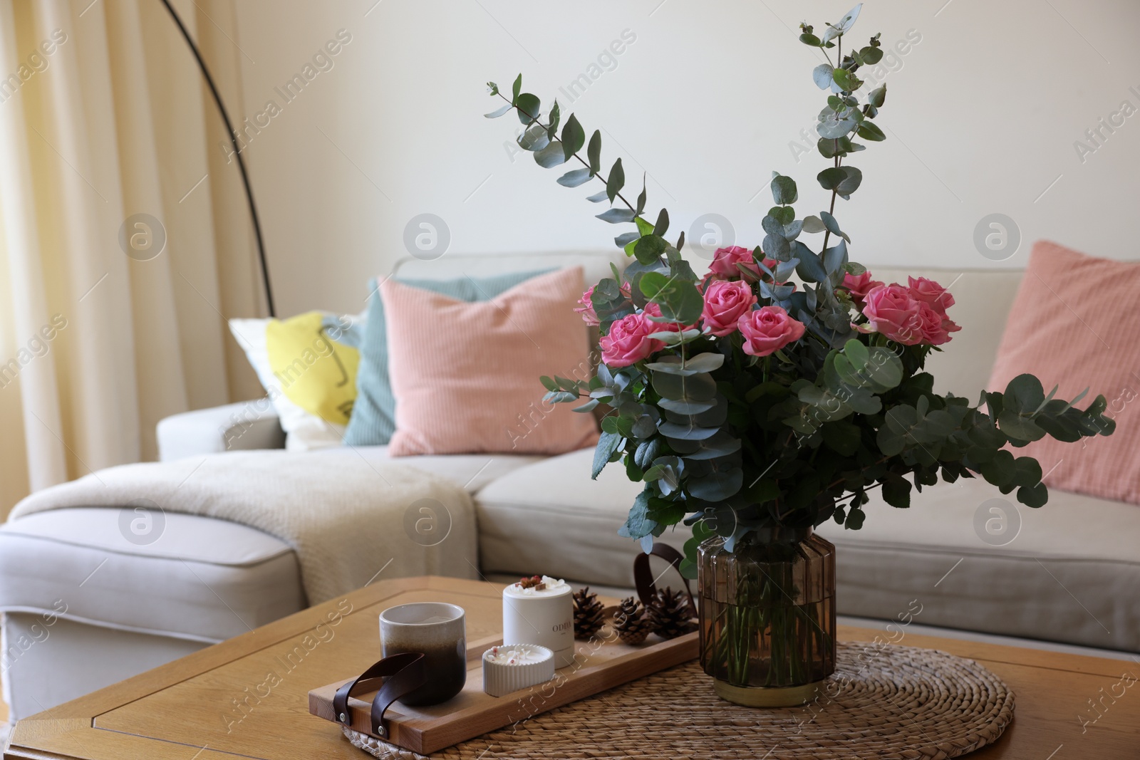 Photo of Beautiful bouquet of roses and eucalyptus branches in vase near candles on table at home. Space for text