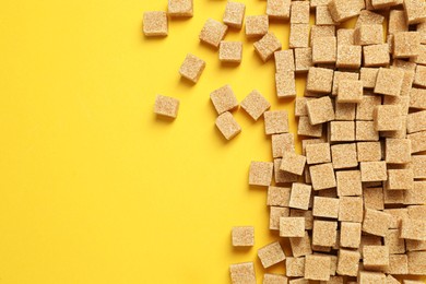 Photo of Brown sugar cubes on yellow background, flat lay. Space for text