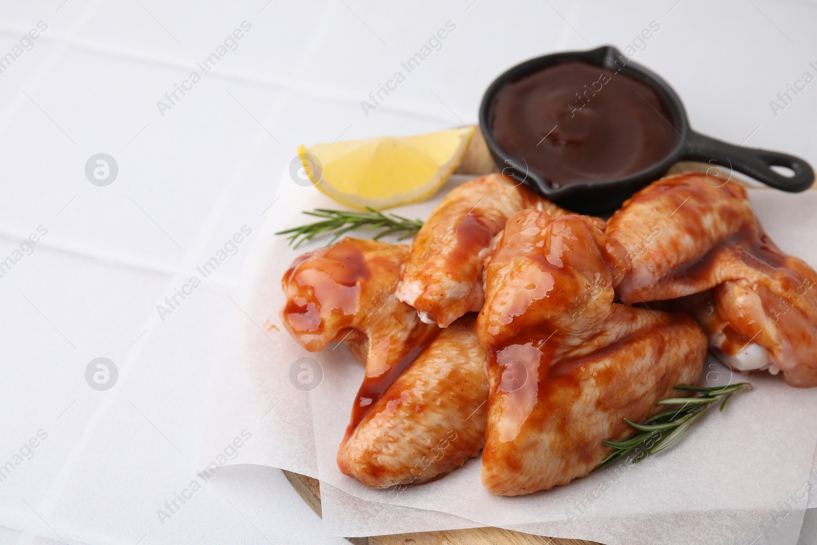 Photo of Raw chicken wings, rosemary, lemon and marinade on light tiled table, closeup. Space for text