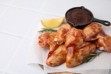 Photo of Raw chicken wings, rosemary, lemon and marinade on light tiled table, closeup. Space for text