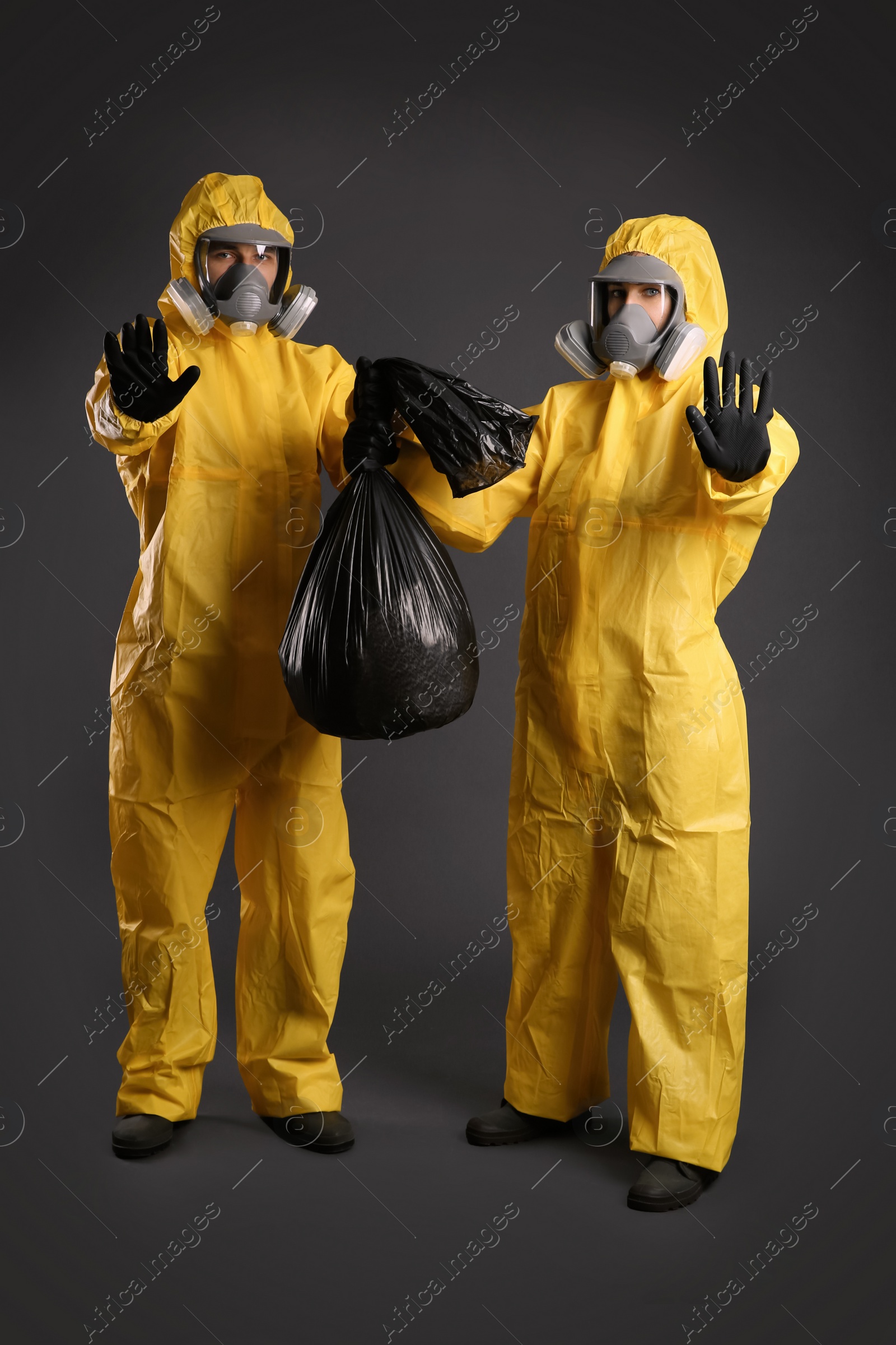 Photo of Man and woman wearing chemical protective suits holding trash bag on grey background. Virus research