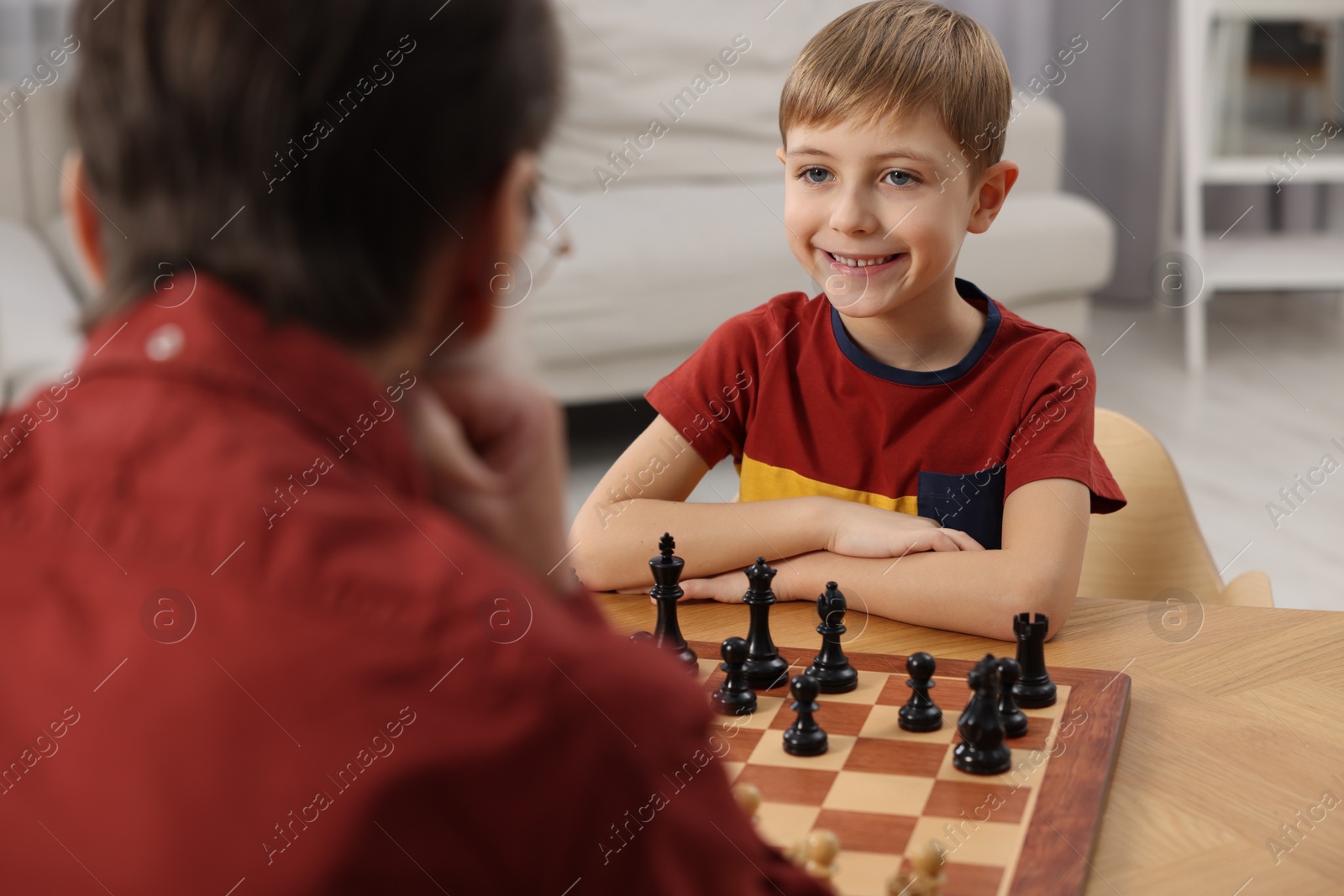 Photo of Little boy playing chess with his grandfather at table in room