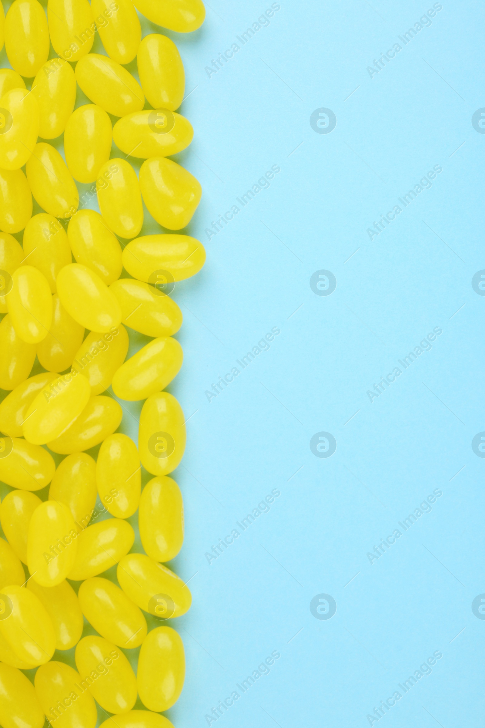 Photo of Many delicious lemon jelly beans on light blue background, flat lay. Space for text