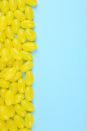 Many delicious lemon jelly beans on light blue background, flat lay. Space for text