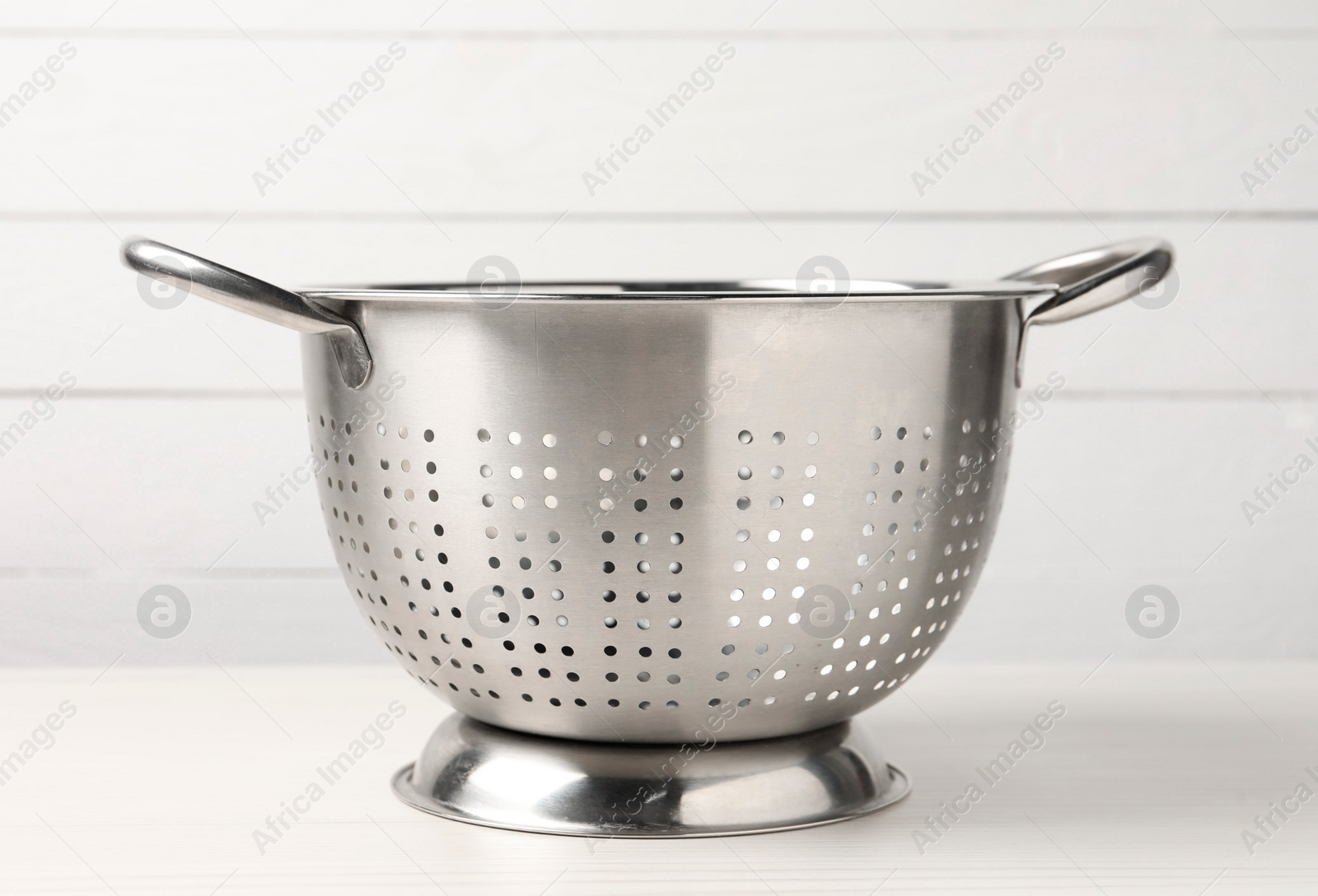 Photo of One metal colander on white wooden table