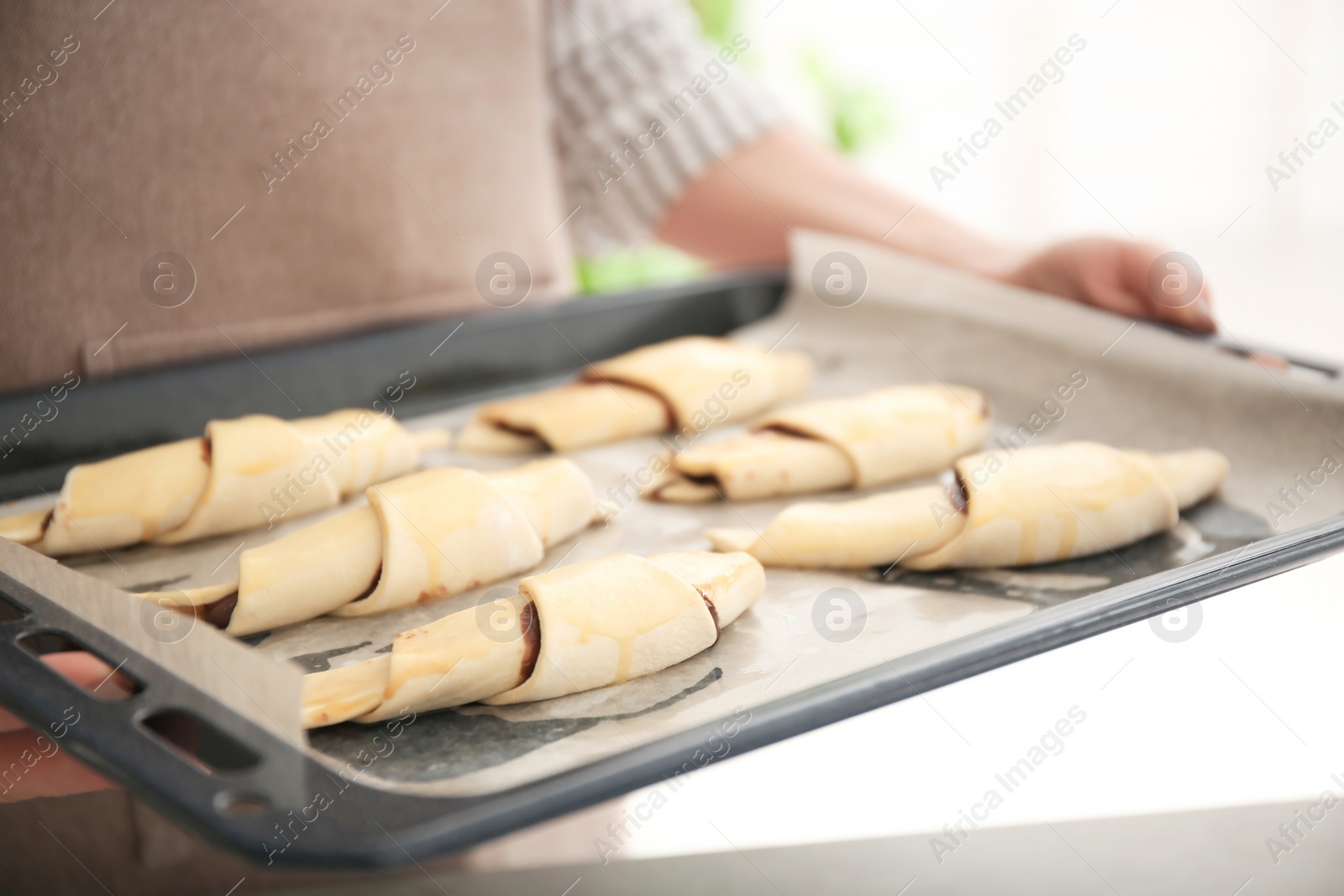 Photo of Woman holding baking sheet with raw croissants indoors
