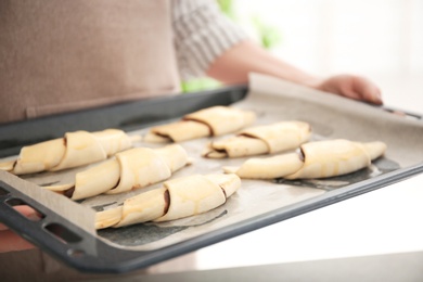 Woman holding baking sheet with raw croissants indoors