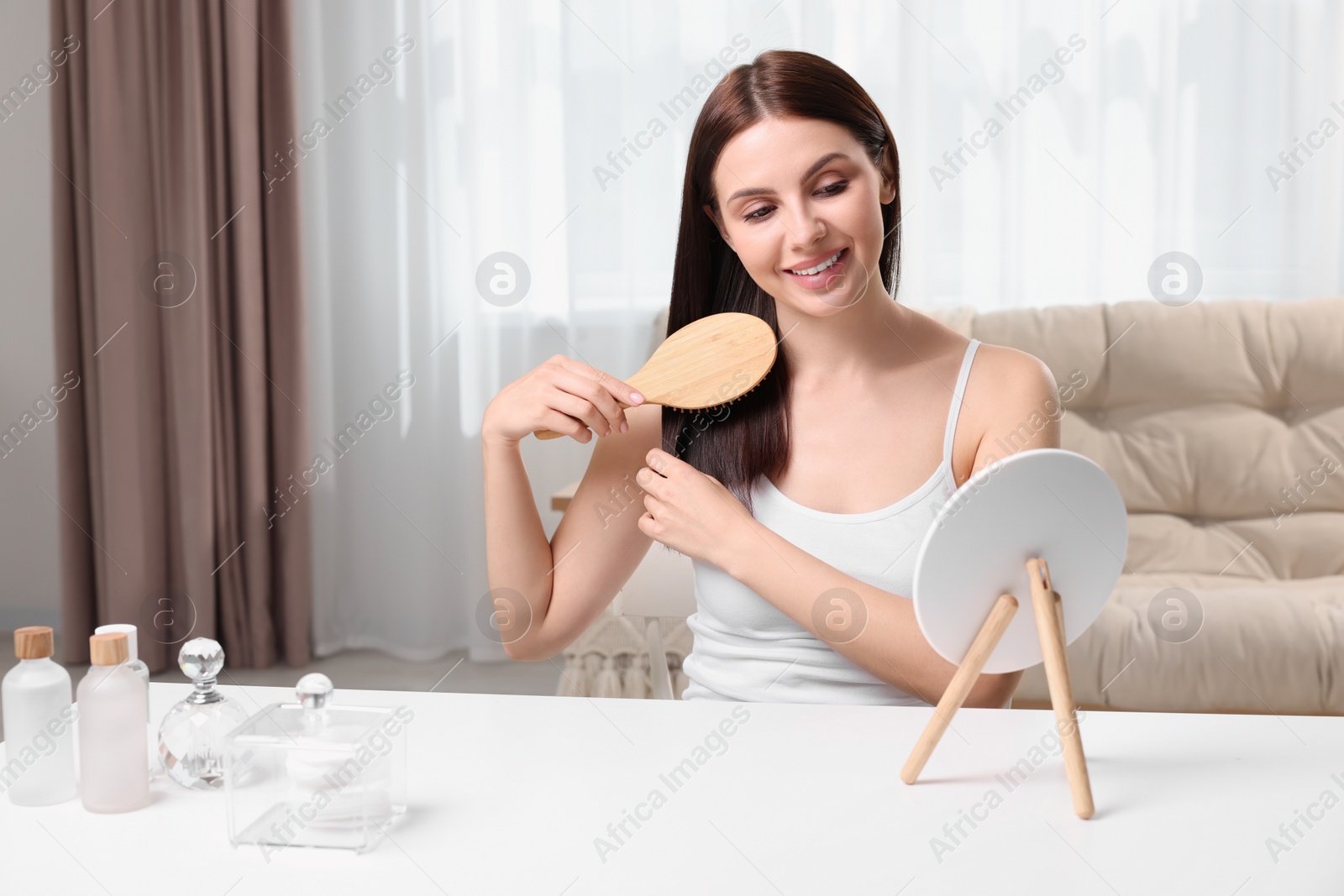 Photo of Beautiful woman brushing her hair near mirror in room, space for text