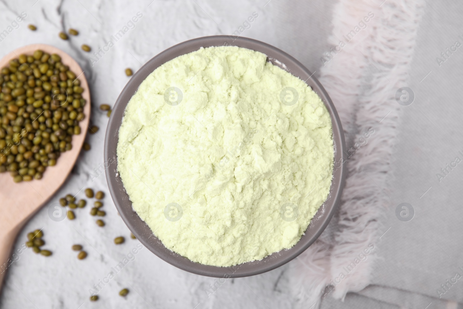 Photo of Mung bean flour in bowl and seeds on white textured table, flat lay