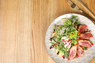 Photo of Delicious salad with roasted duck breast served on wooden table, flat lay. Space for text