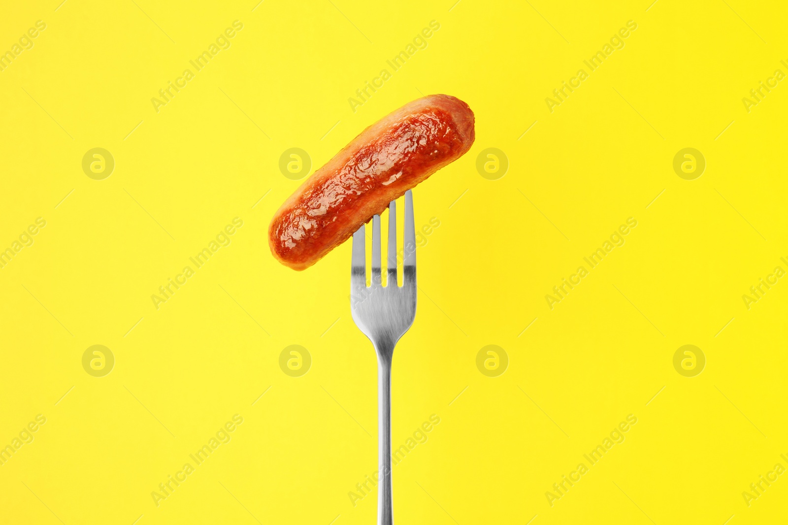 Photo of Fork with tasty fried sausage on yellow background
