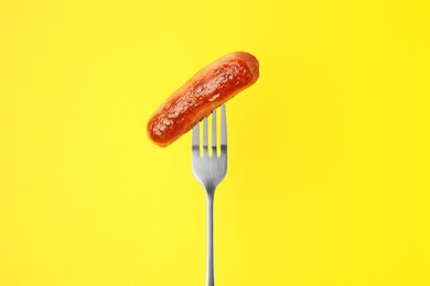 Fork with tasty fried sausage on yellow background