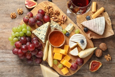 Flat lay composition with board of delicious cheese and snacks on wooden background