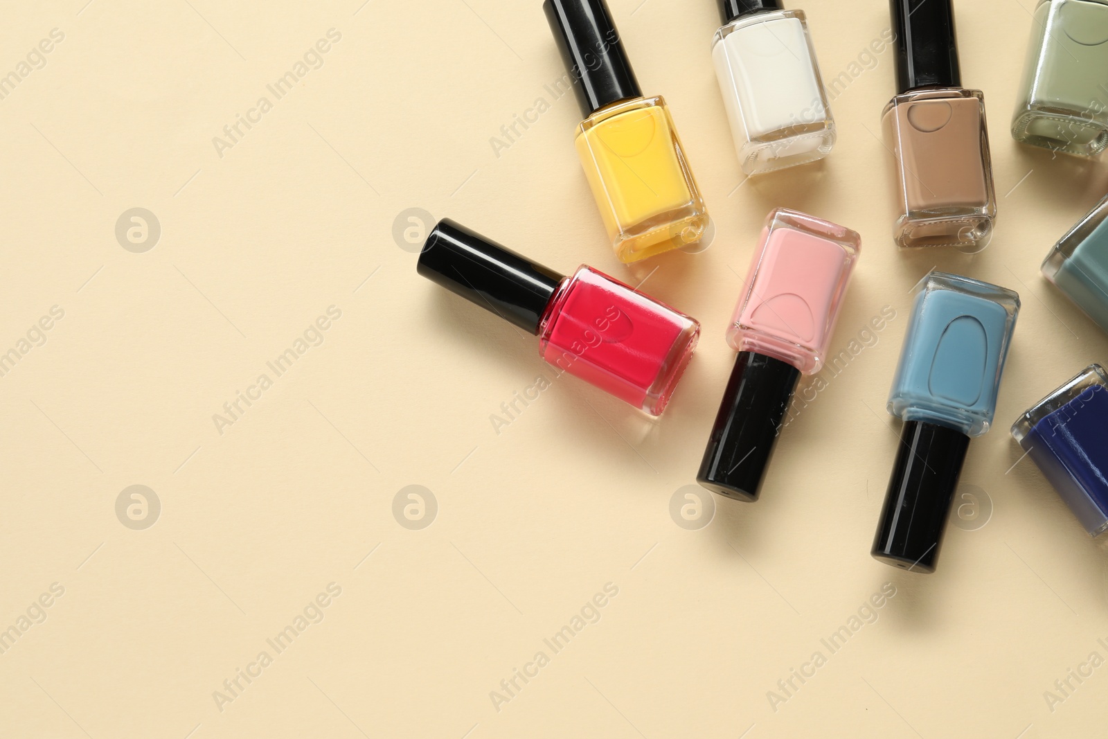 Photo of Colorful nail polishes in bottles on beige background, flat lay. Space for text