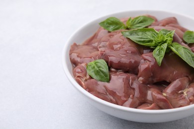 Photo of Bowl with raw chicken liver and basil on white table, closeup. Space for text