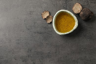 Photo of Fresh truffles and oil in bowl on grey table, flat lay. Space for text