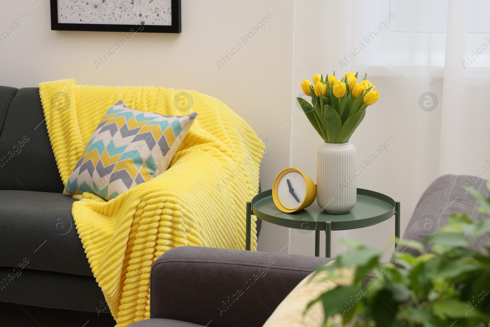 Photo of Spring atmosphere. Stylish living room interior with comfortable furniture and bouquet of beautiful yellow tulips