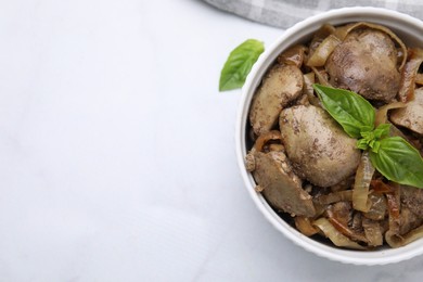 Photo of Delicious fried chicken liver with onion and basil in bowl on white table, top view. Space for text