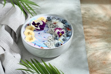 Delicious smoothie bowl with fresh fruits, blueberries and flowers on color textured table. Space for text