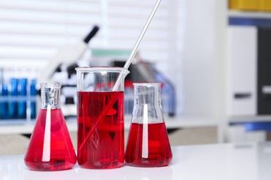 Photo of Laboratory analysis. Different glassware with red liquid on white table indoors. Space for text