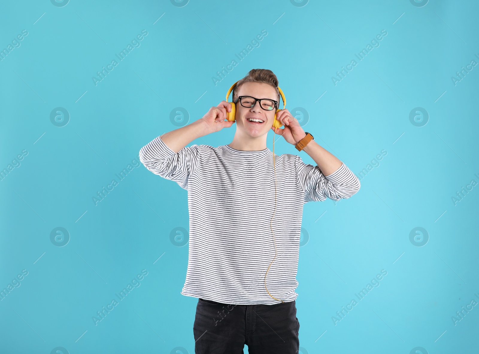 Photo of Handsome teenage boy in glasses with headphones on color background