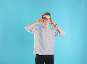 Handsome teenage boy in glasses with headphones on color background