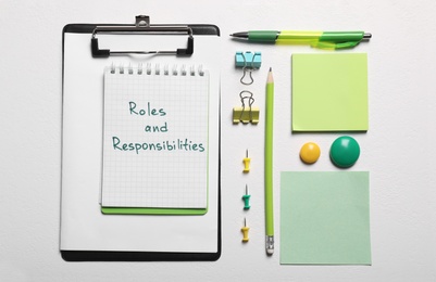 Notebook with phrase Roles And Responsibilities near office supplies on white table, flat lay