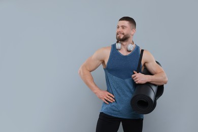 Handsome man with fitness mat and headphones on grey background, space for text