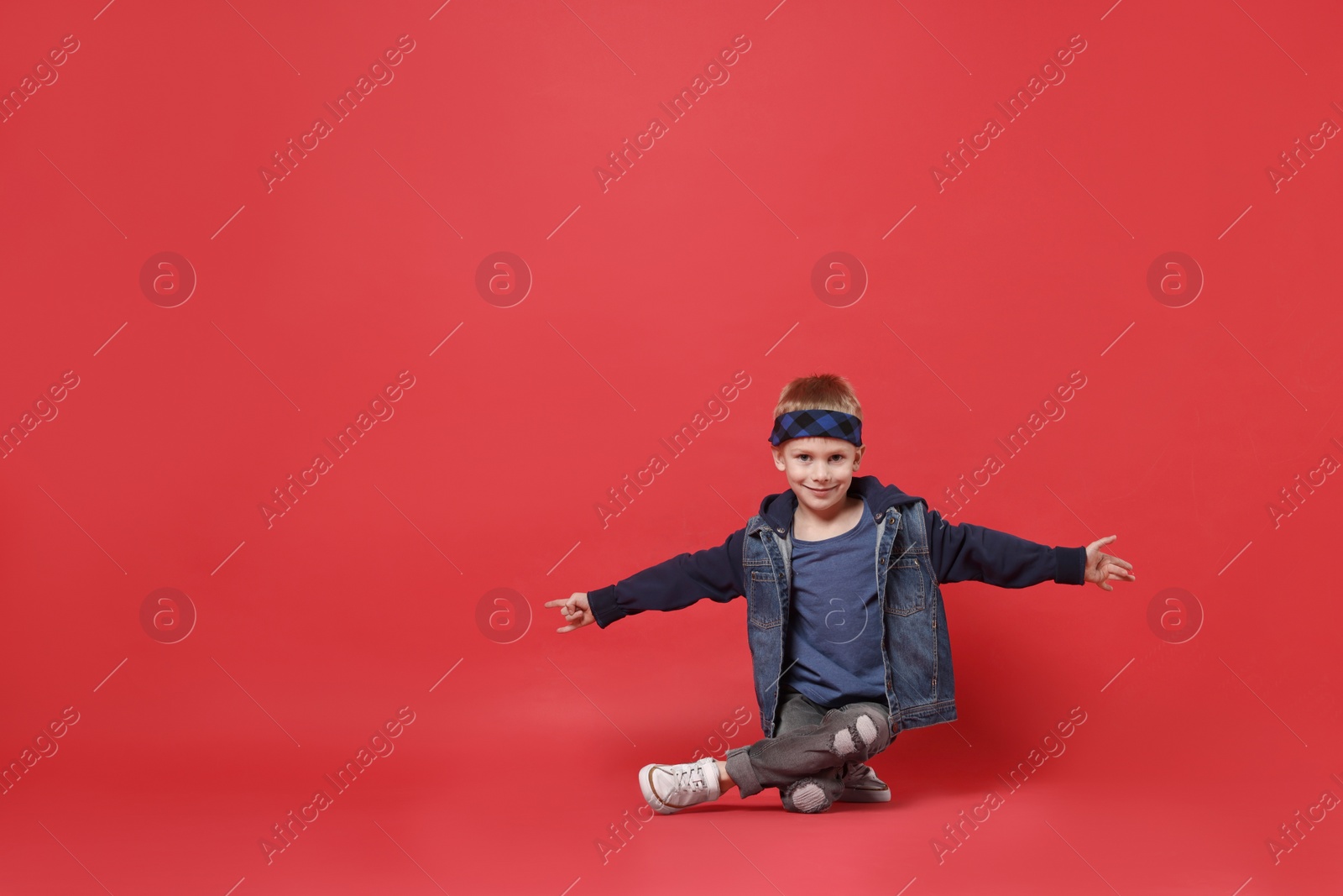 Photo of Happy little boy dancing on red background. Space for text