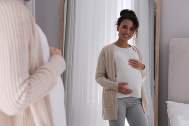 Pregnant young African-American woman near mirror at home