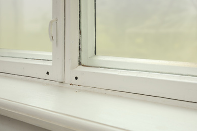 Old window with white wooden sill in room, closeup