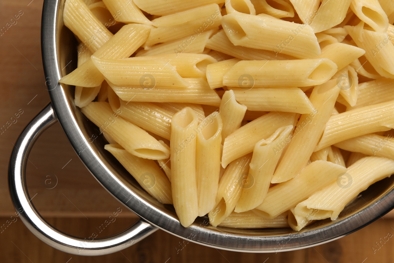 Photo of Cooked pasta in metal colander on wooden table, top view