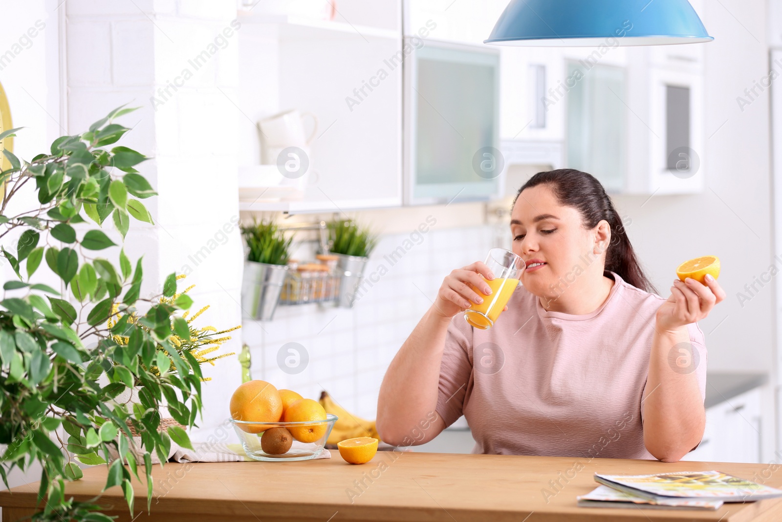Photo of Overweight woman drinking fresh juice and orange in kitchen. Healthy diet