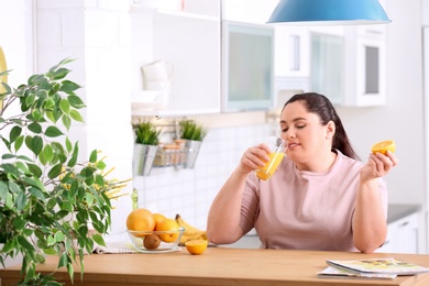 Overweight woman drinking fresh juice and orange in kitchen. Healthy diet