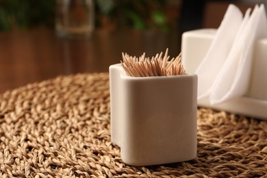 Photo of Wooden holder with many toothpicks on wicker mat, closeup. Space for text