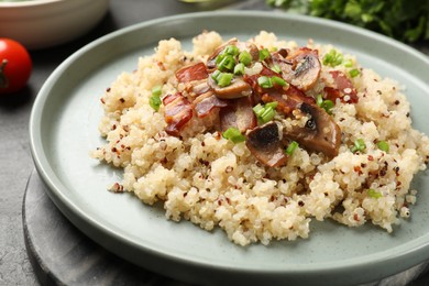 Photo of Plate of tasty quinoa porridge with fried bacon, mushrooms and green onion on table, closeup