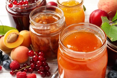 Photo of Jars with different jams and fresh fruits on white wooden table, closeup