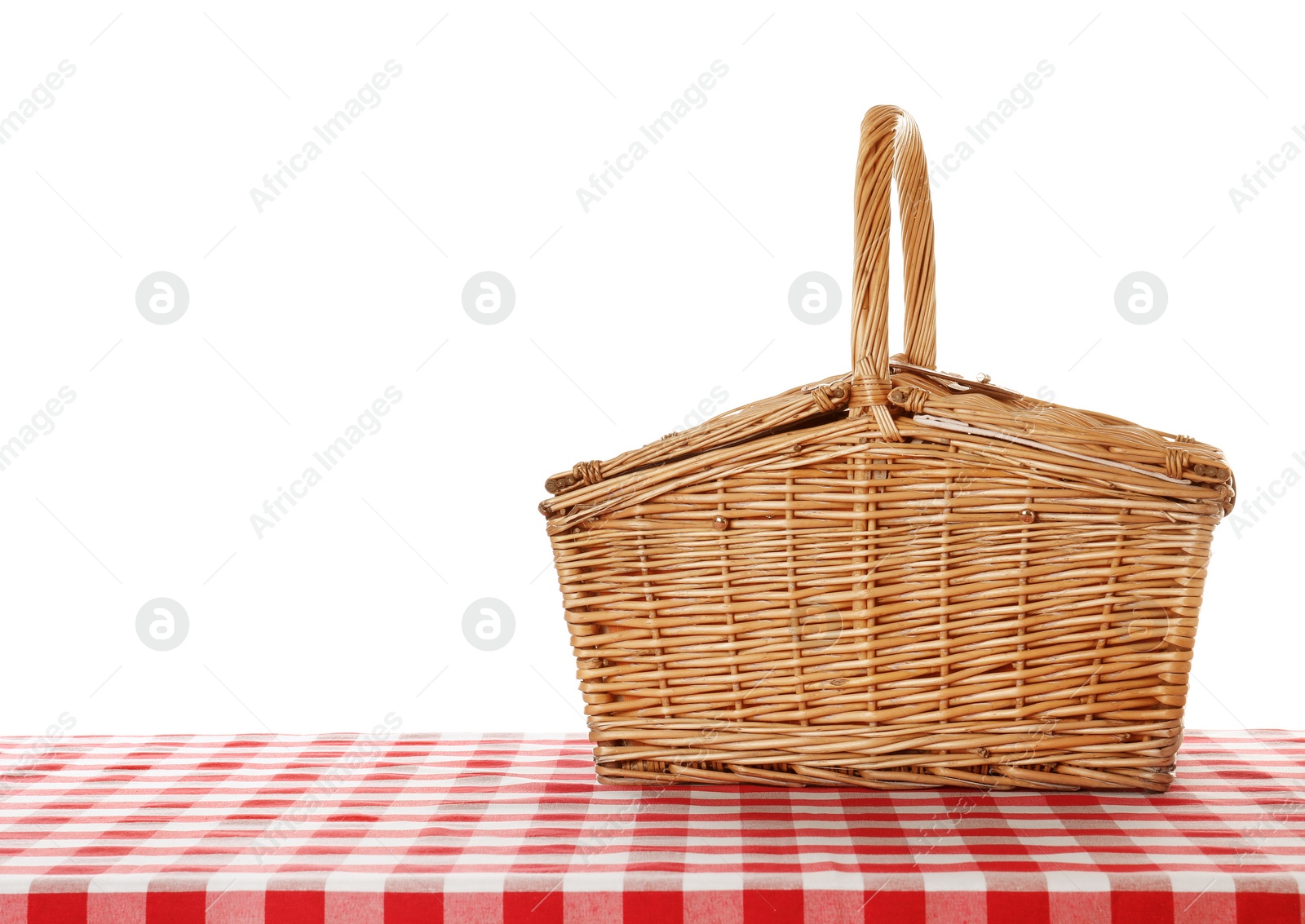 Photo of Closed wicker picnic basket on checkered tablecloth against white background