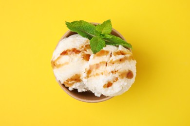 Scoops of tasty ice cream with caramel sauce and mint leaves on yellow background, top view