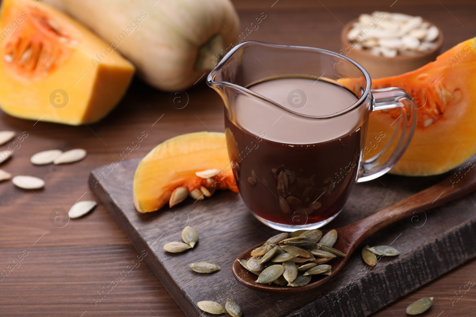 Photo of Fresh pumpkin seed oil in glass pitcher on wooden table. Space for text