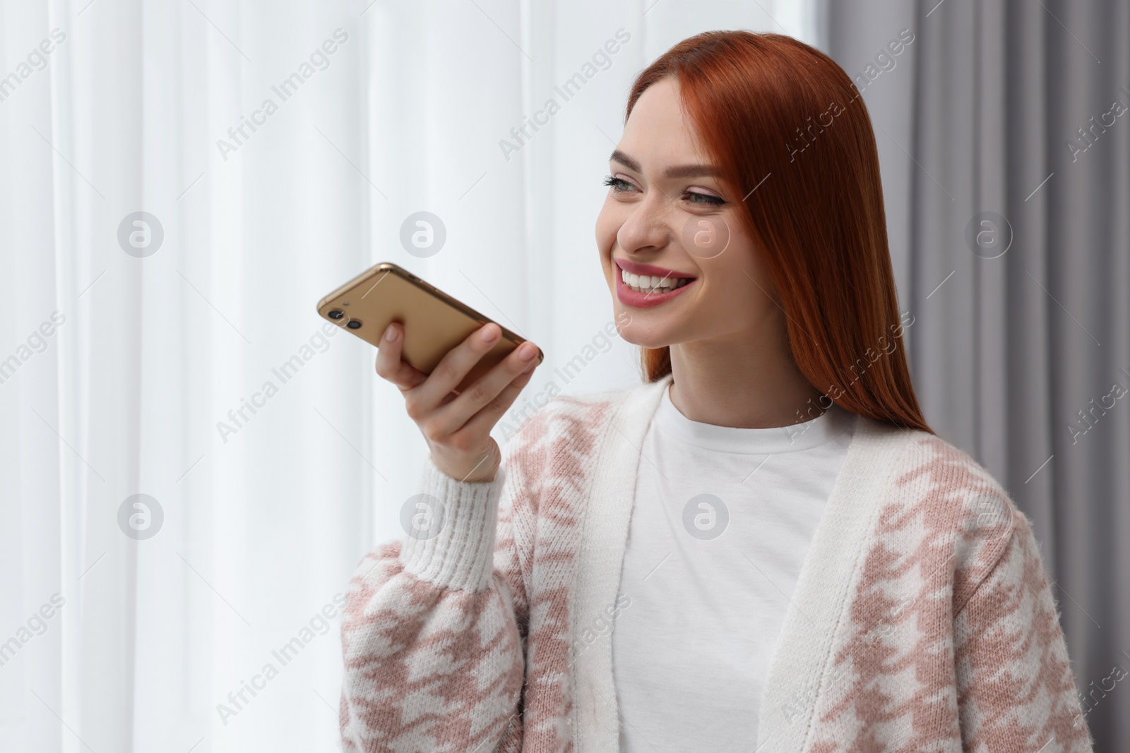 Photo of Happy woman sending voice message via smartphone at home